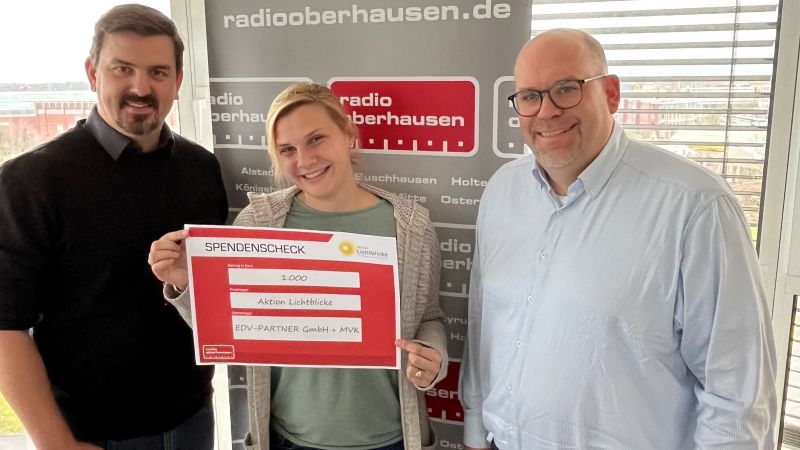 Bastian Schumacher, Geschäftsführer von EDV-PARTNER, Veit Kuhl, Geschäftsführer von der MVK GmbH und die Reporterin von Radio Oberhausen halten gemeinsam einen Spendencheck über 1000 €, adressiert an die Aktion Lichtblicke