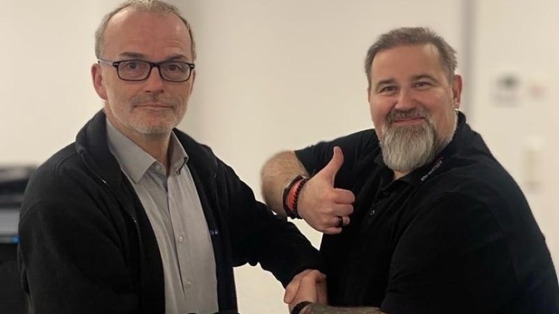 Thomas Schnieber und Thorsten Lübke, die Mitarbeiter des Jahres 2023, schütteln sich die Hand. Thorsten zeigt zusätzlich einen Daumen nach oben.