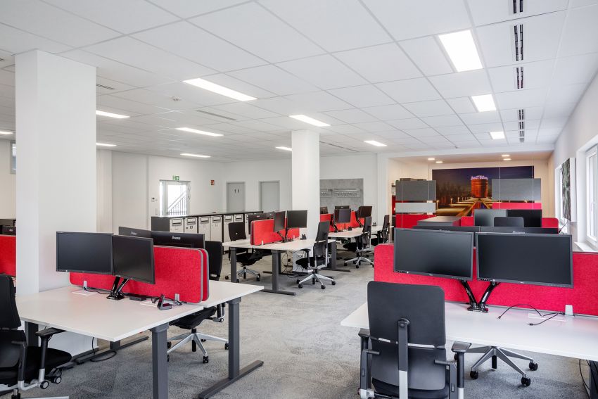 Modernes Büro mit vielen Arbeitsflächen, mehreren beweglichen hüfthohen Schränken und einer offenen Küche im Hintergrund.