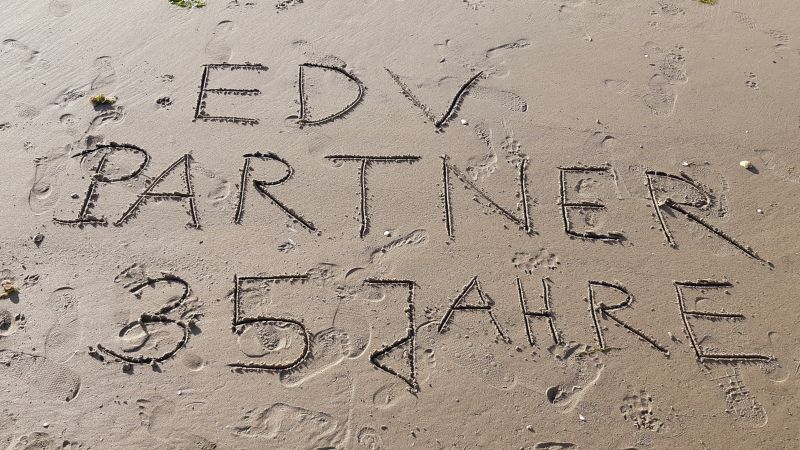 Zu sehen ist ein Foto, auf dem im feuchten Sand ‚EDV-PARTNER 35 Jahre‘ eingezeichnet ist.